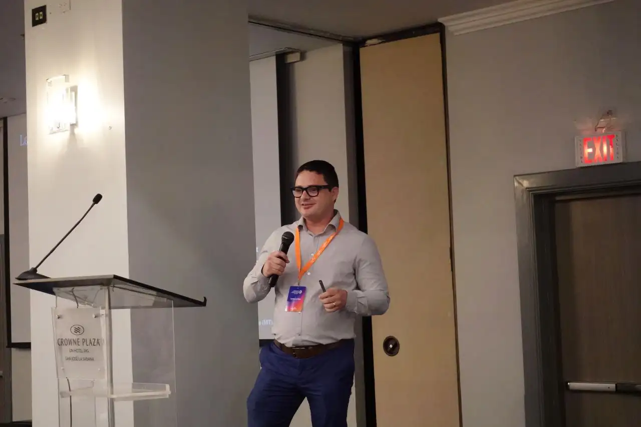 Carlos Rojas speaking with a handheld microphone beside a lectern